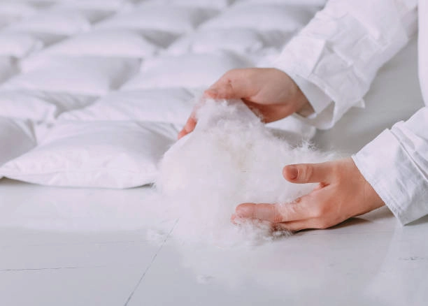 Hands holding fluffy down filling for a mattress topper.”